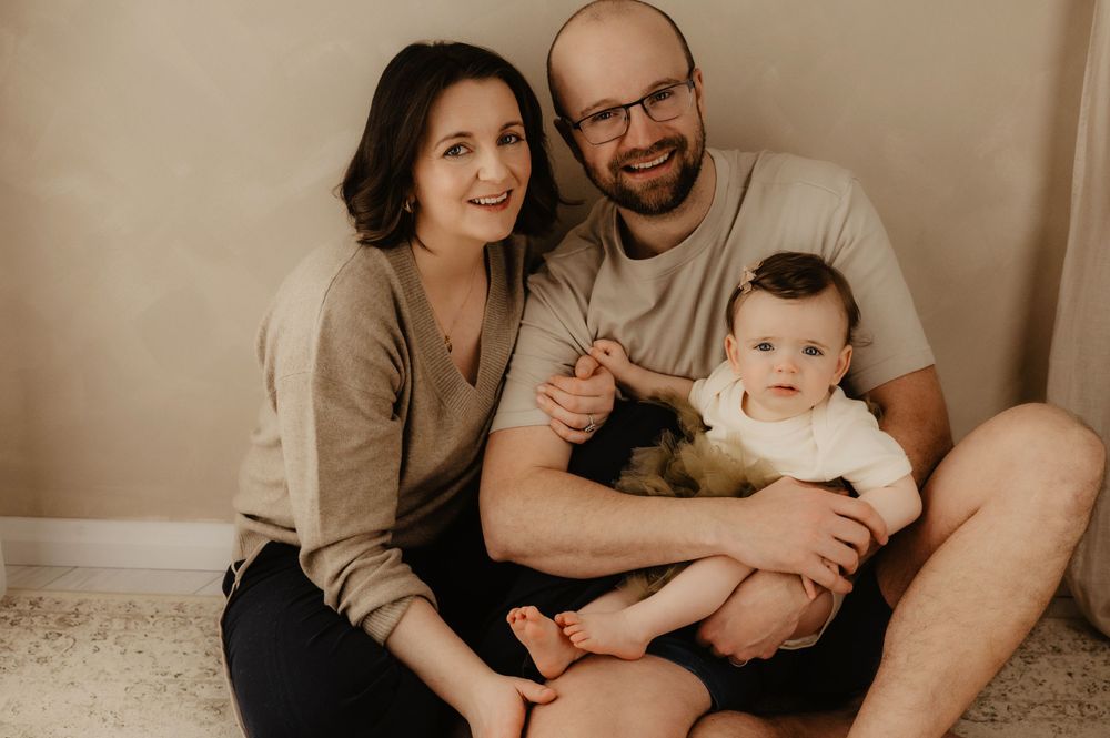 Loving family sits together on carpet for a warm portrait session in neutral tones.