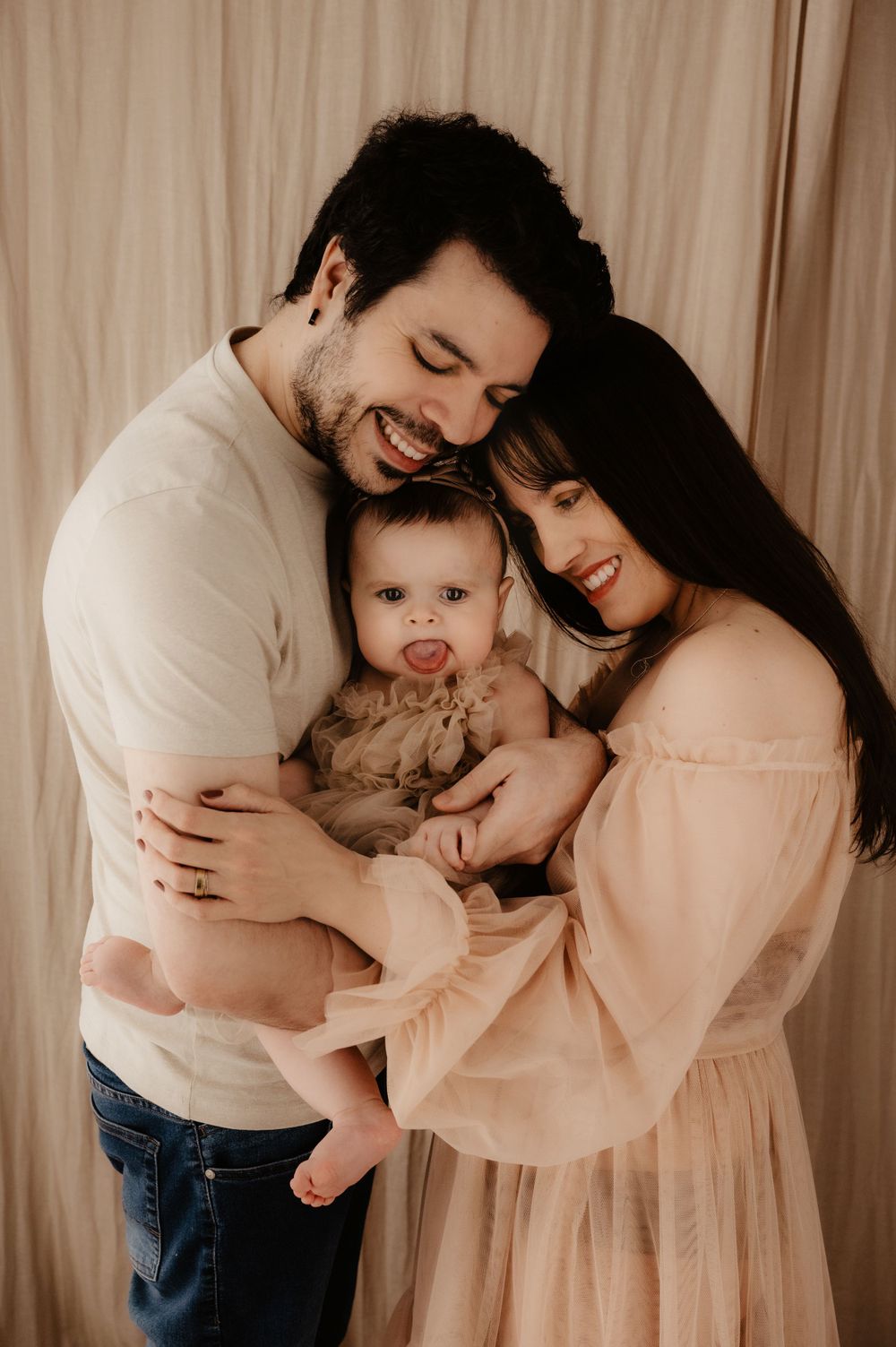 A tender family moment captured in warm tones as parents share joyful laughs while holding their baby.