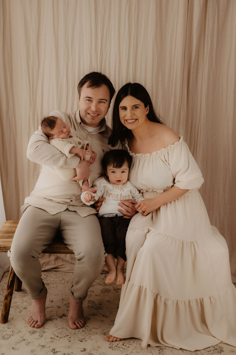 A family portrait in soft neutral tones against a beige backdrop.