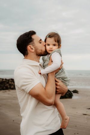 Sweet moment between parent and child on overcast beach with rocky coastline.