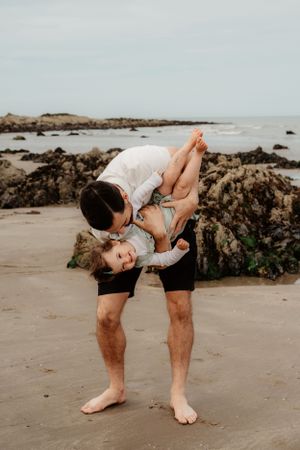 A playful moment captured on a rocky beach as one person dips another near the shore.