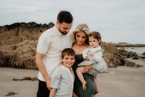 Family of four poses together on rocky beach at sunset.