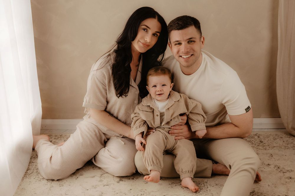 Family of three in matching neutral outfits sitting together on floor for portrait session.