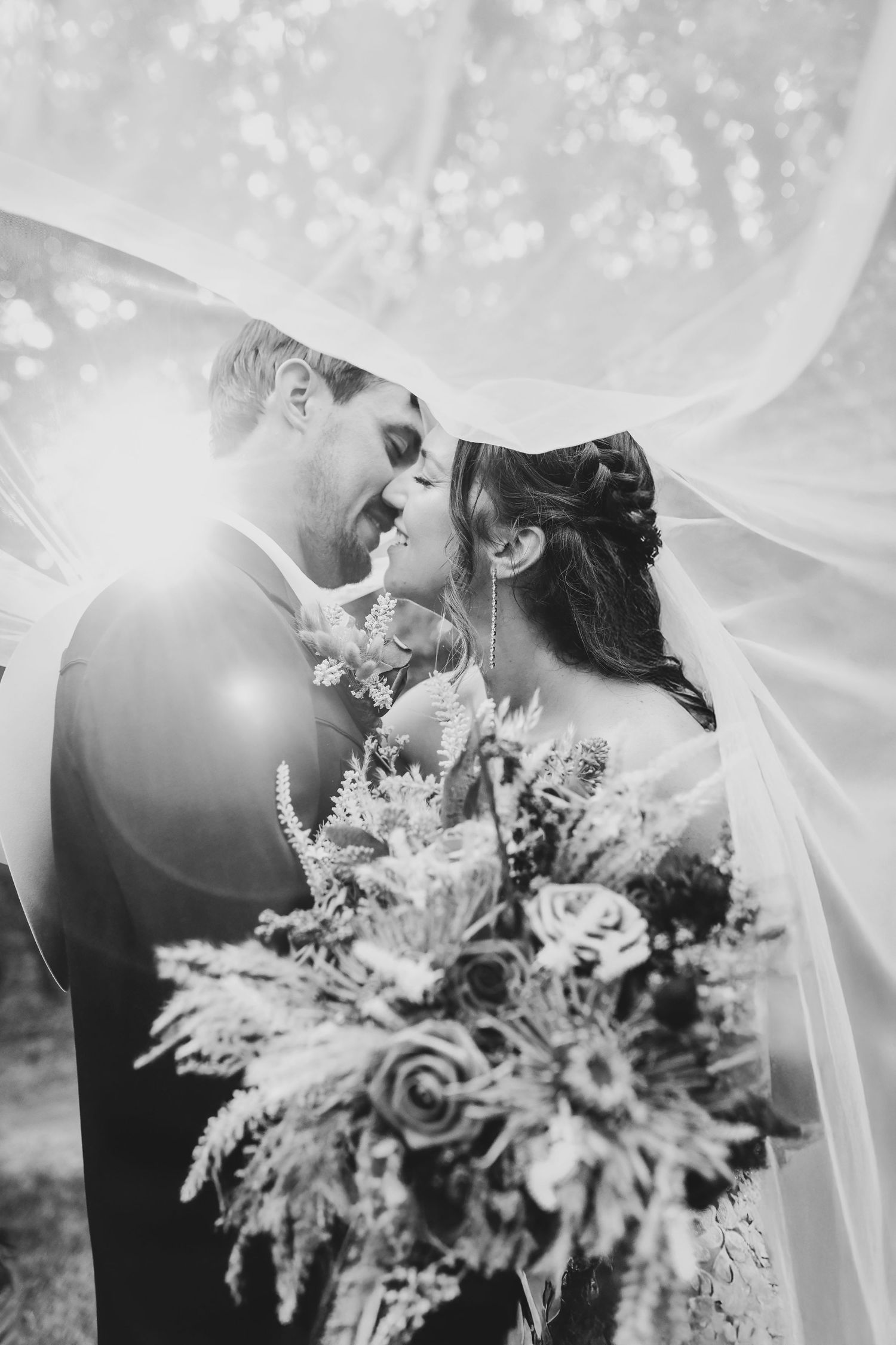 Bride and groom kissing beneath a veil at sunset at whispering oaks