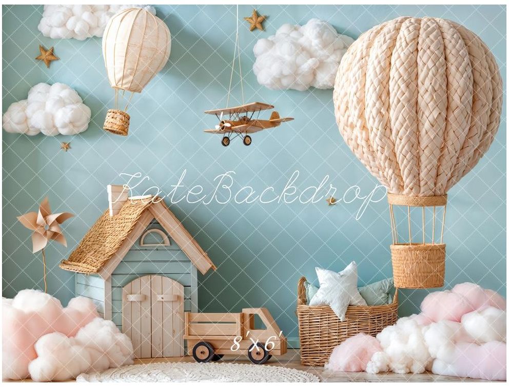 Whimsical baby shower backdrop featuring hot air balloons, clouds, a toy plane, and a cottage in soft pastel tones.