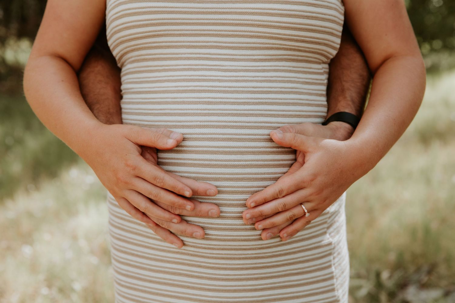 Close-up view of hands gently cradling a pregnant belly wearing a striped maternity shirt.