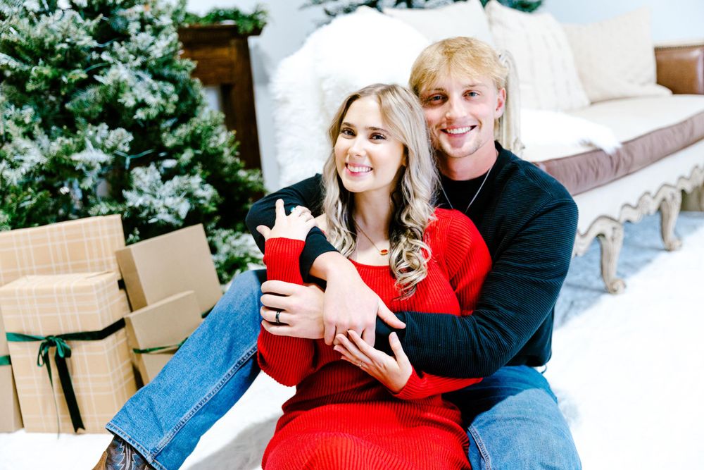 A couple in festive attire sits together on outdoor steps with moving boxes nearby during the holiday season.