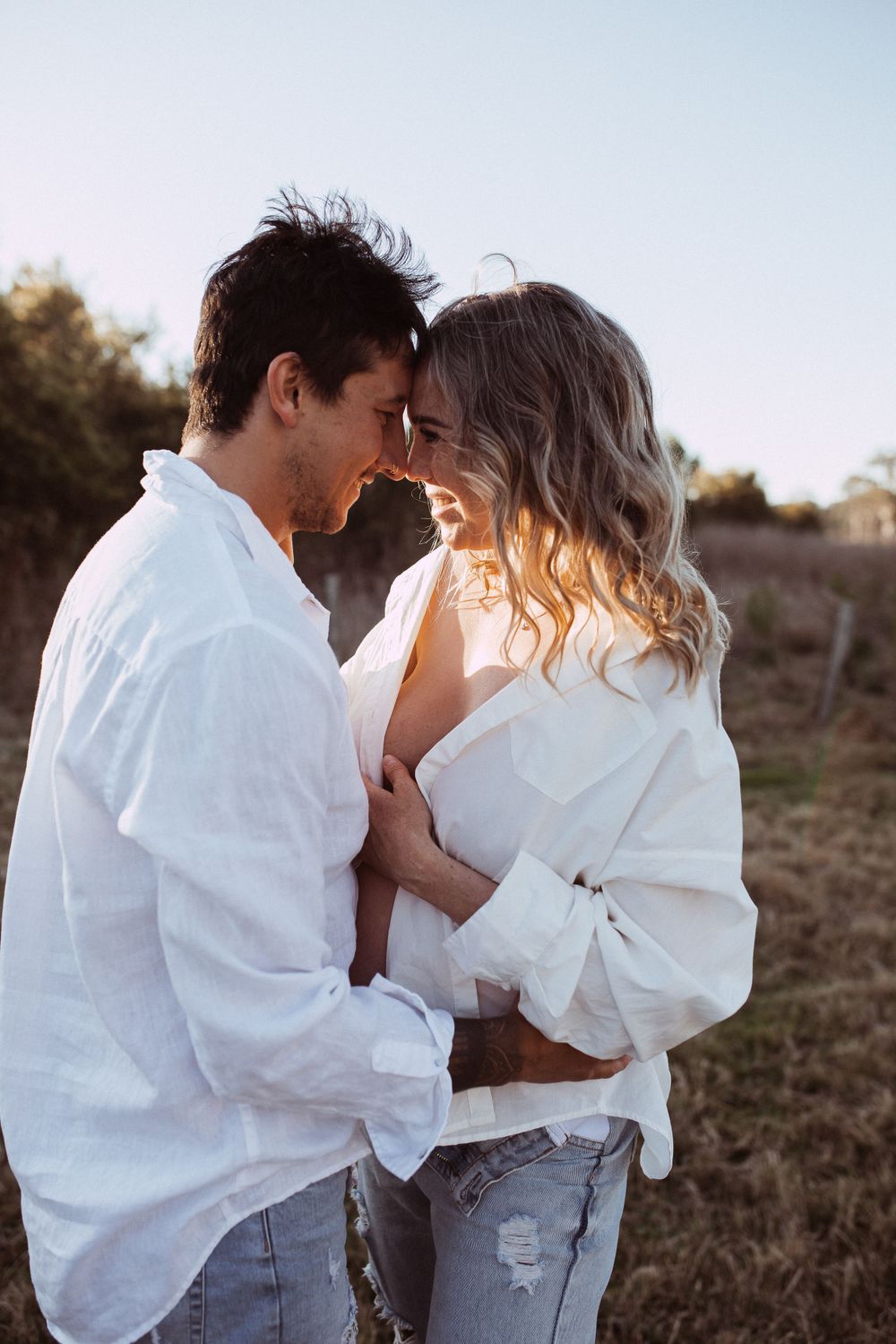 A romantic outdoor portrait of a couple in white shirts sharing an intimate moment during golden hour.