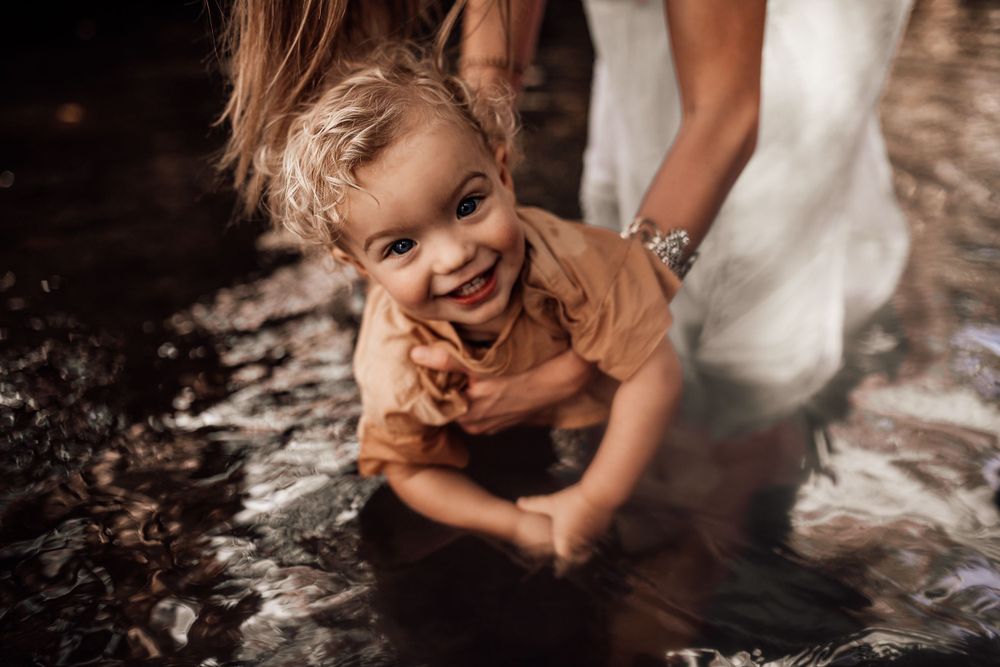 A child in a brown shirt crawls on the ground while smiling and playing in the dirt.