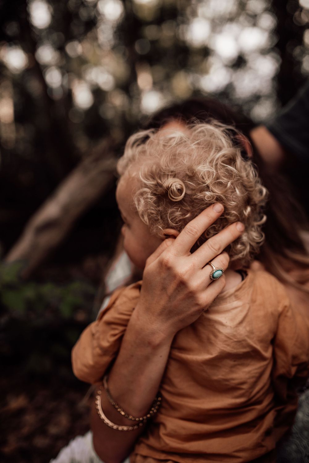 Close-up artistic photo showing curly blonde hair and a gentle hand with a ring in warm natural lighting.