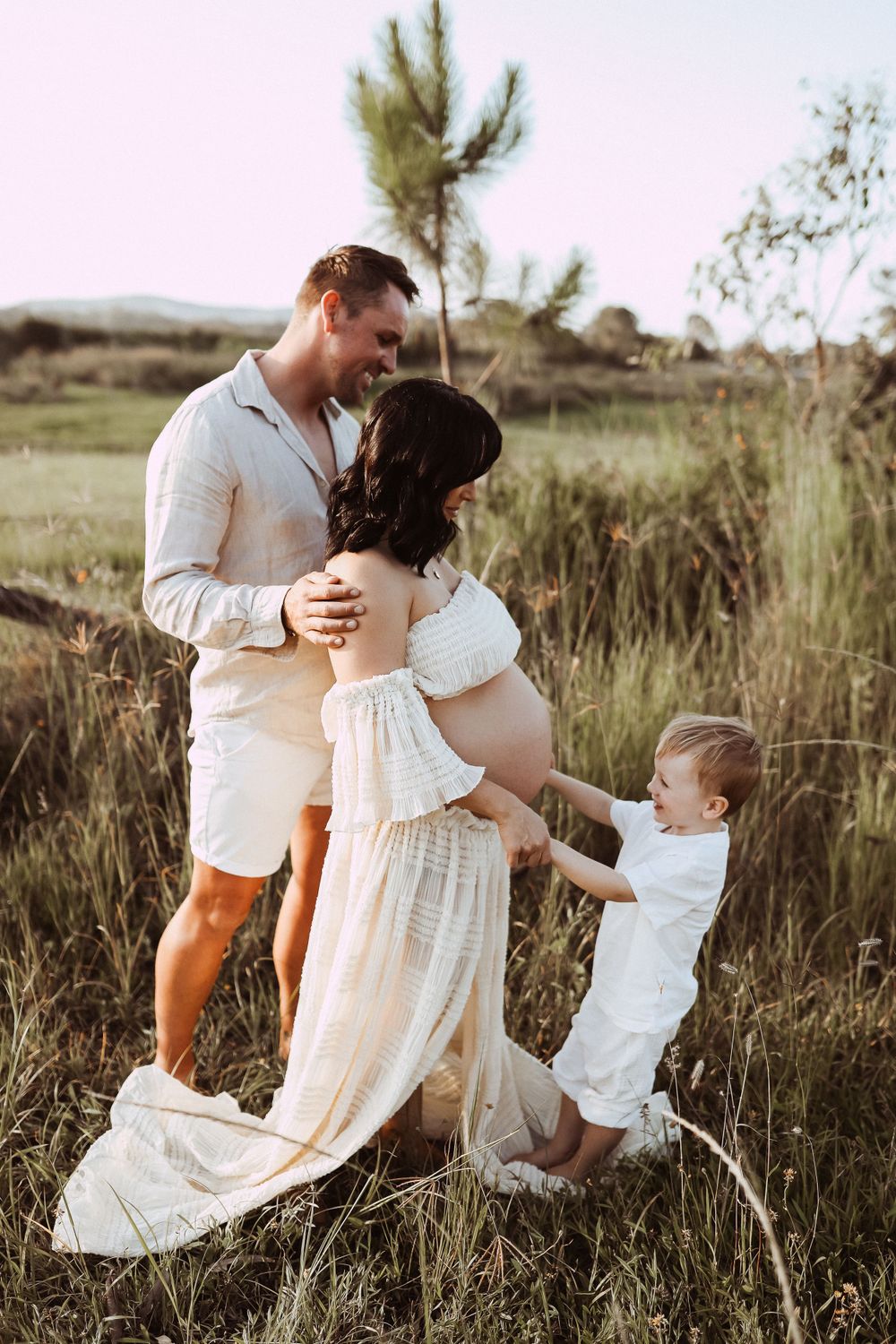 Candid family portrait in natural setting with tall grass and pine trees.