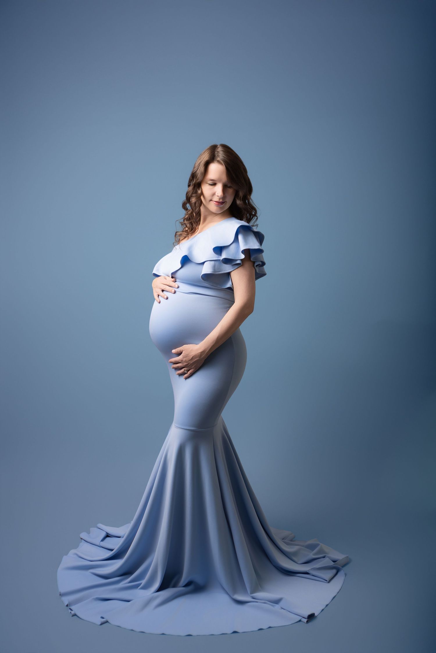 A maternity photo series showing a flowing light blue dress against a navy backdrop in four elegant poses.