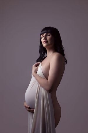 Artistic boudoir photograph series of figure in flowing white fabric against moody gray background.
