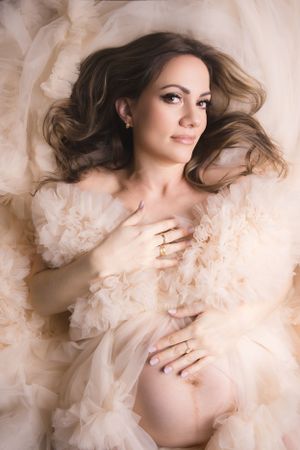 An ethereal maternity photo with soft cream tulle fabric and delicate styling shot from above.