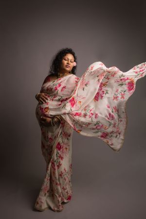 Flowing floral dress with billowing fabric creates ethereal maternity portrait against dark backdrop.