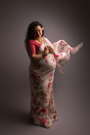 Elegant maternity pose with flowing pink floral dress fabric in motion against neutral background.