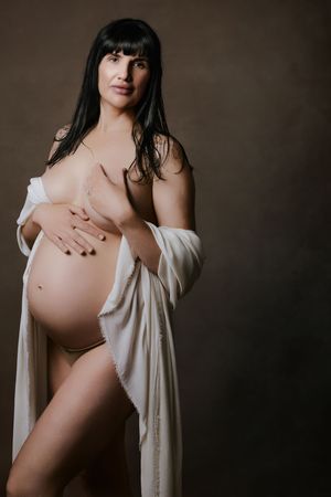 Artistic maternity photo featuring an expectant mother in a white robe against a dark background. The wet look maternity
