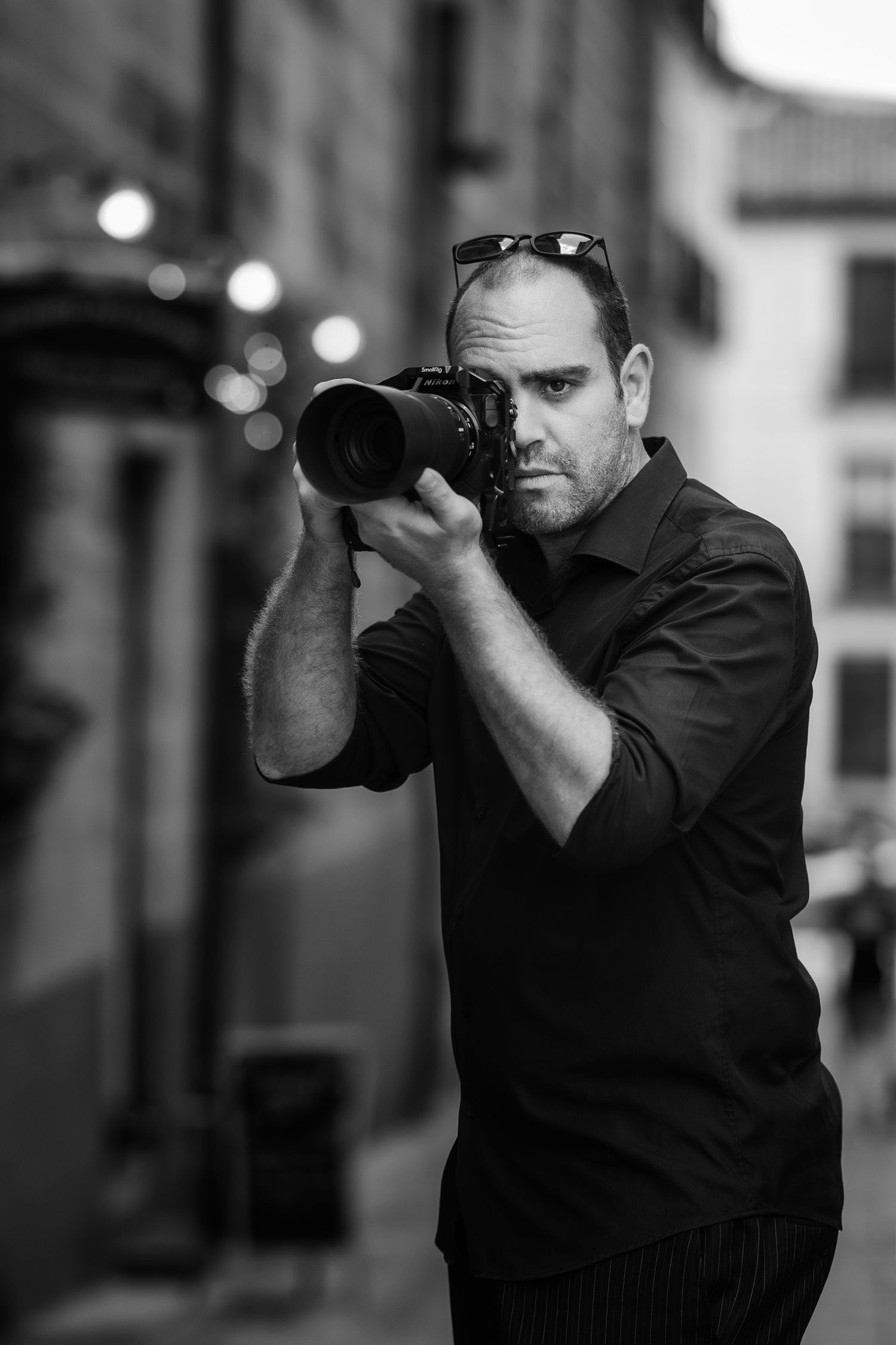 Black and white photo of photographer using professional camera on urban street.