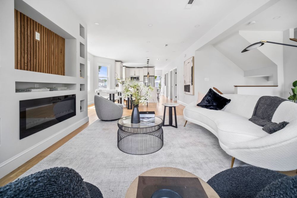 Modern living room with white curved sofa, sleek fireplace, built-in shelves, and stylish coffee table on a neutral area rug.