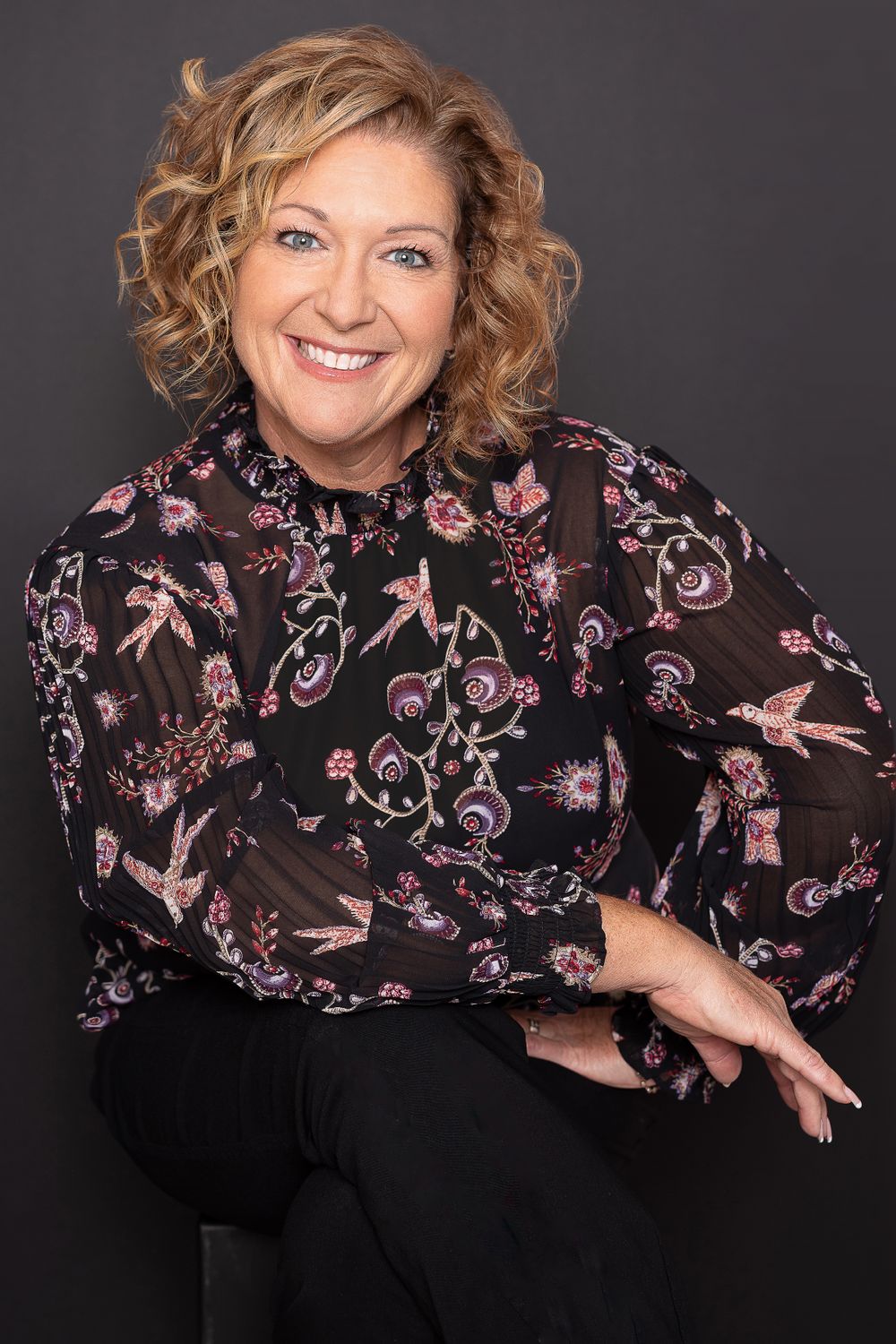 Studio portrait featuring black floral blouse with pink bird pattern against dark background.