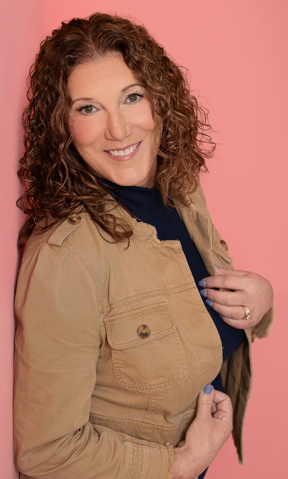 Portrait in tan utility jacket against coral background with natural curly hair styling.