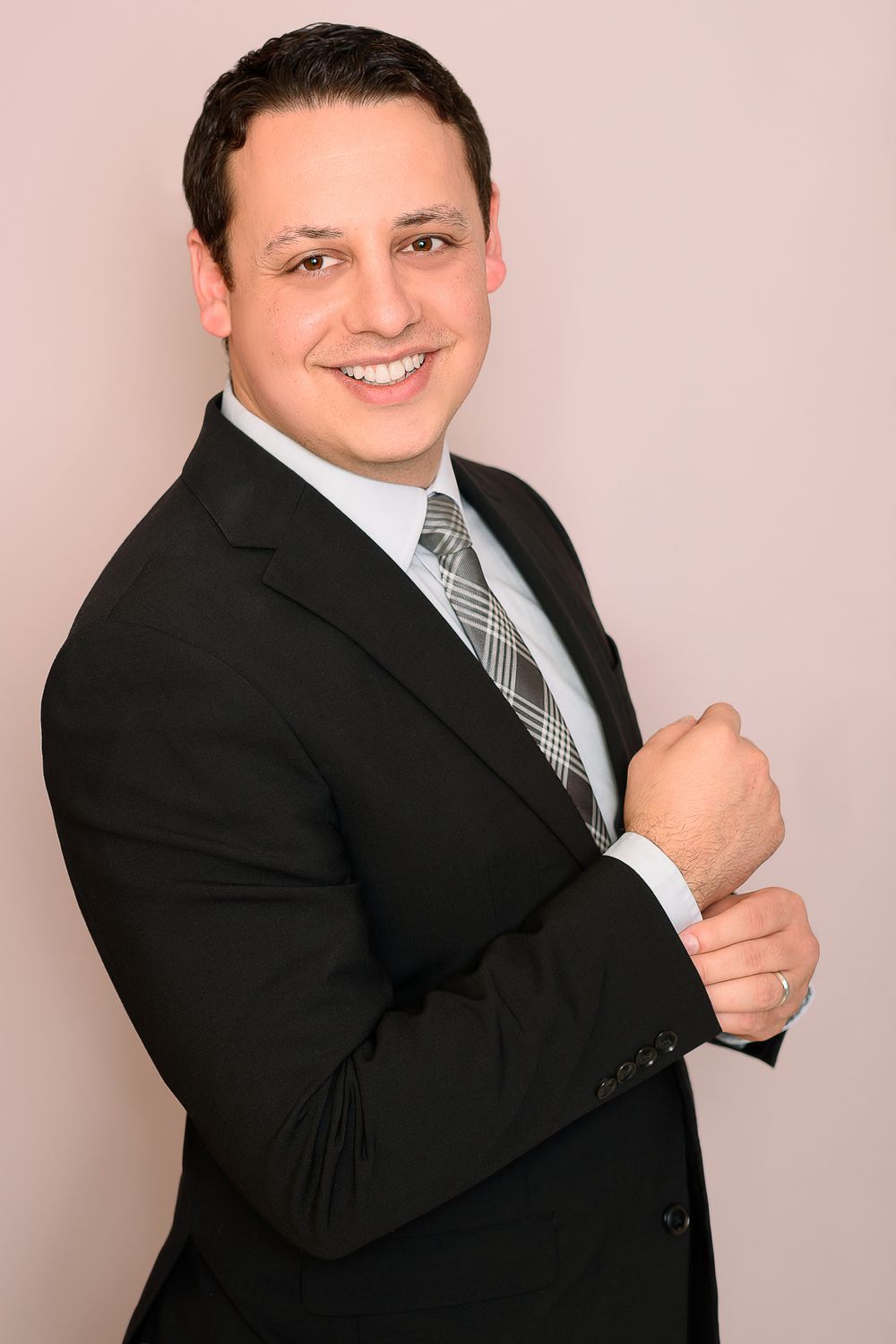 Professional headshot of someone in a dark suit and striped tie against a pink background.