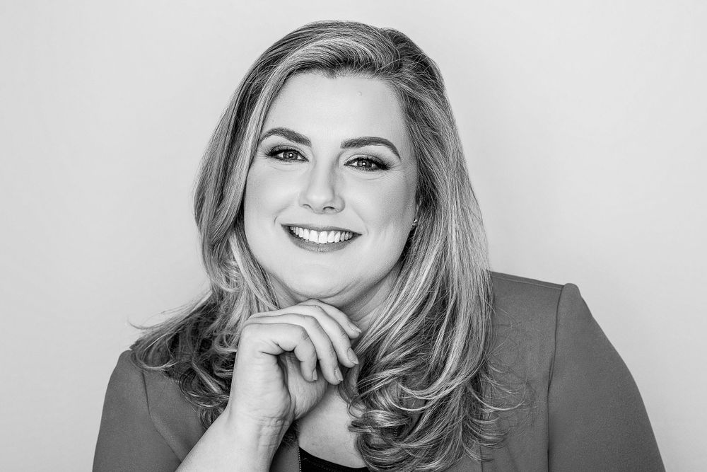 Black and white professional headshot of someone with styled hair resting chin on hand.