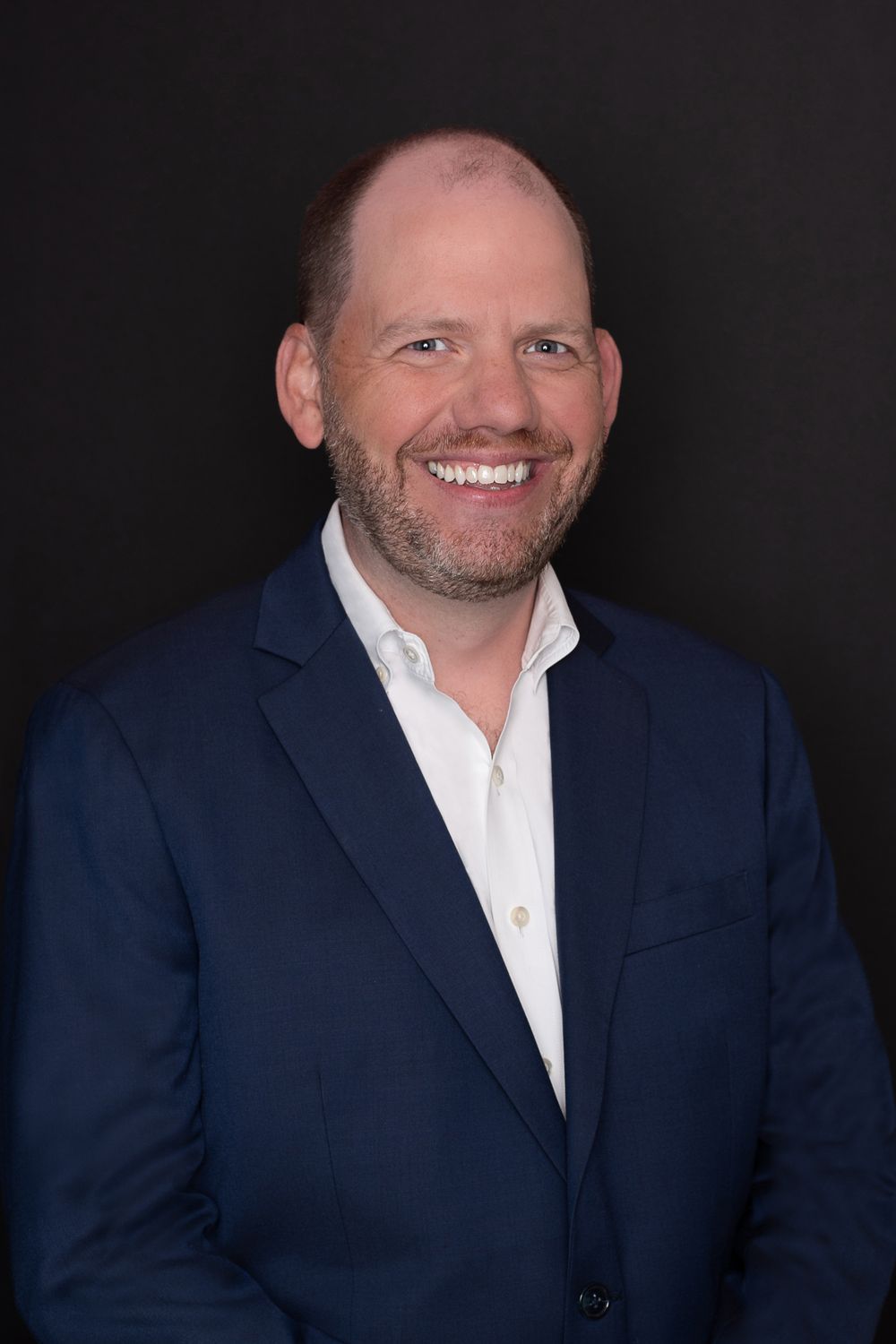 Business portrait of someone in a navy blazer and white shirt against a dark background.