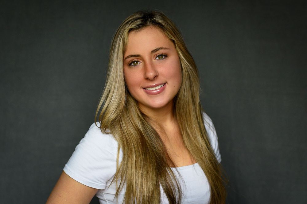 Casual portrait of someone with long blonde hair wearing a white top against a dark background.