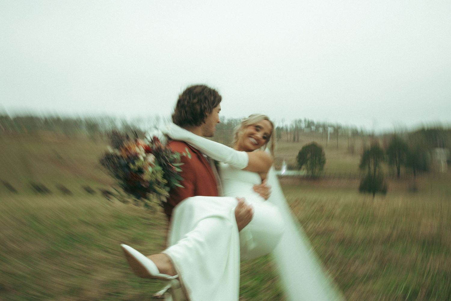 A romantic wedding couple embraces in brick doorway with vintage lanterns hanging in foreground.