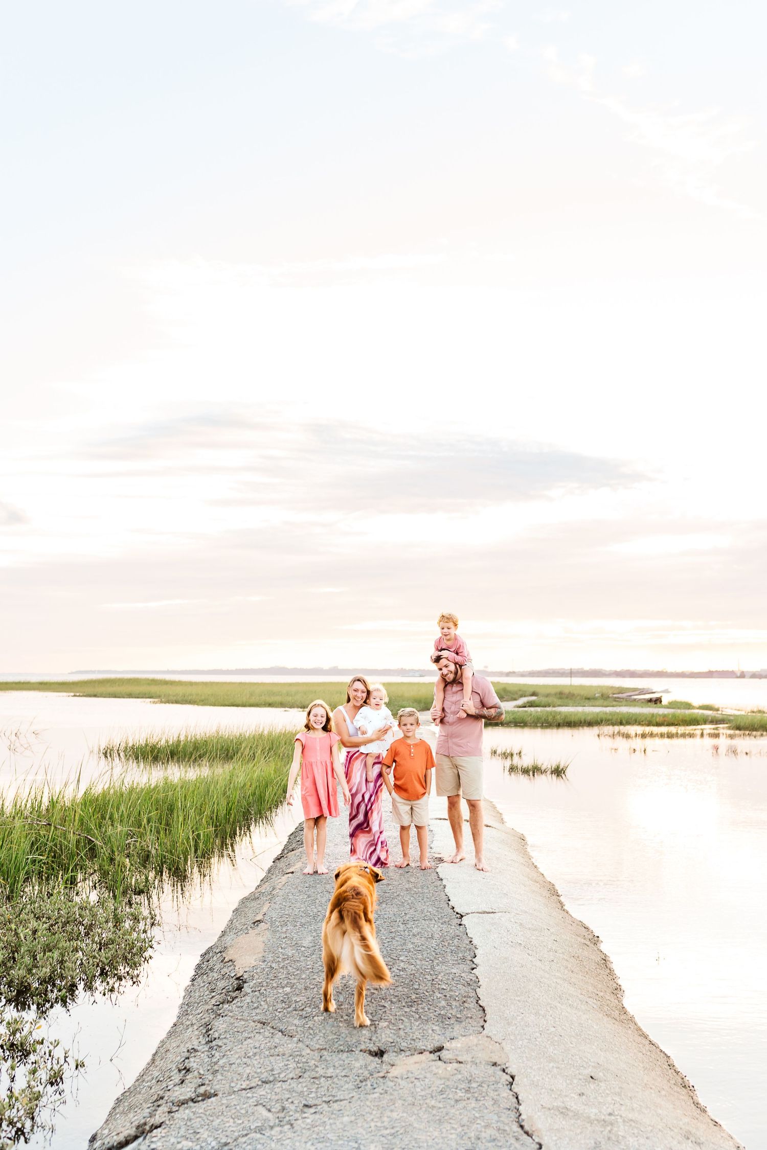 Family walking together on a coastal path surrounded by marsh grass at sunset. PRESLEY ROSE PHOTOGRAPHY OCEAN ISLE BEACH SUNSET BEACH