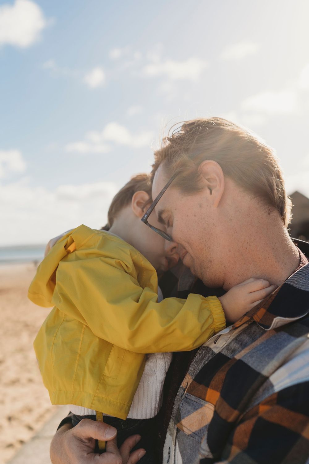 A tender moment shared between parent and child on a sunny beach, with the child wearing a bright yellow jacket.