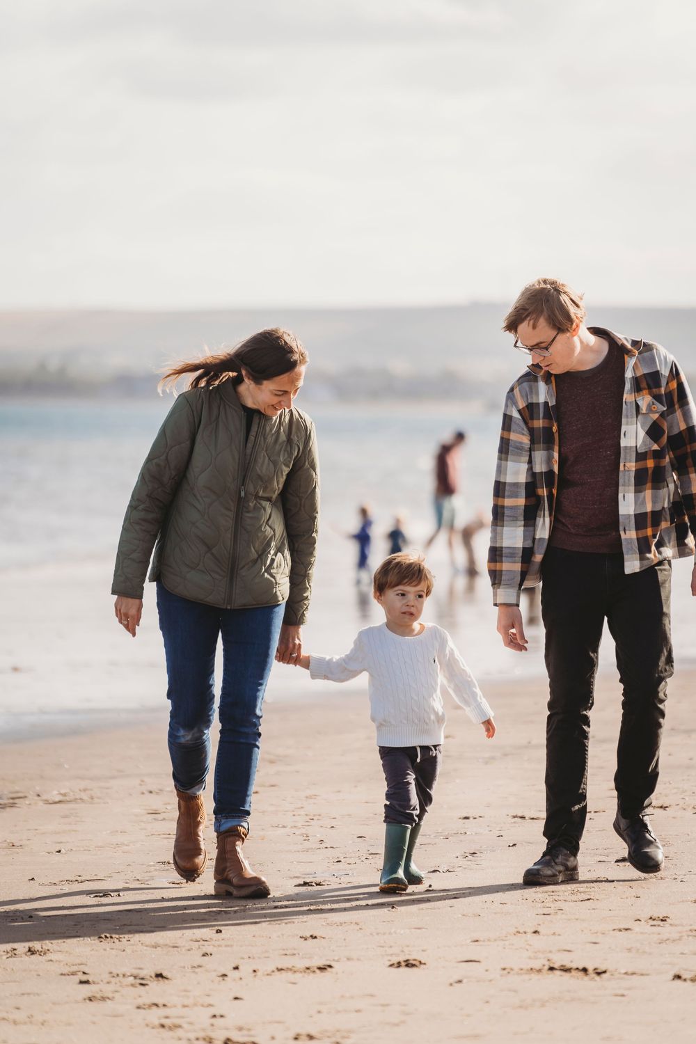 Family walking together on a sandy beach during sunset while holding hands and making footprints in the sand.