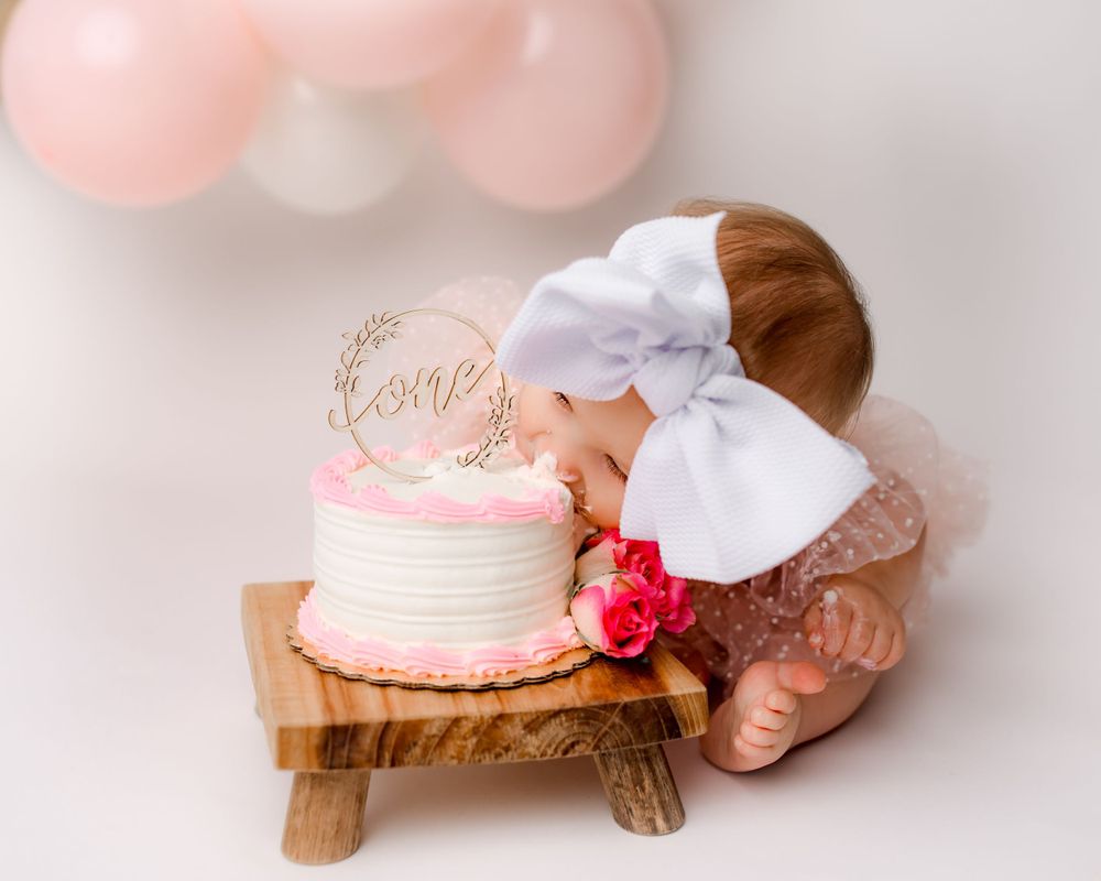 Baby girl eating first birthday cake with pink balloons and bow | Pittsburgh luxury cake smash