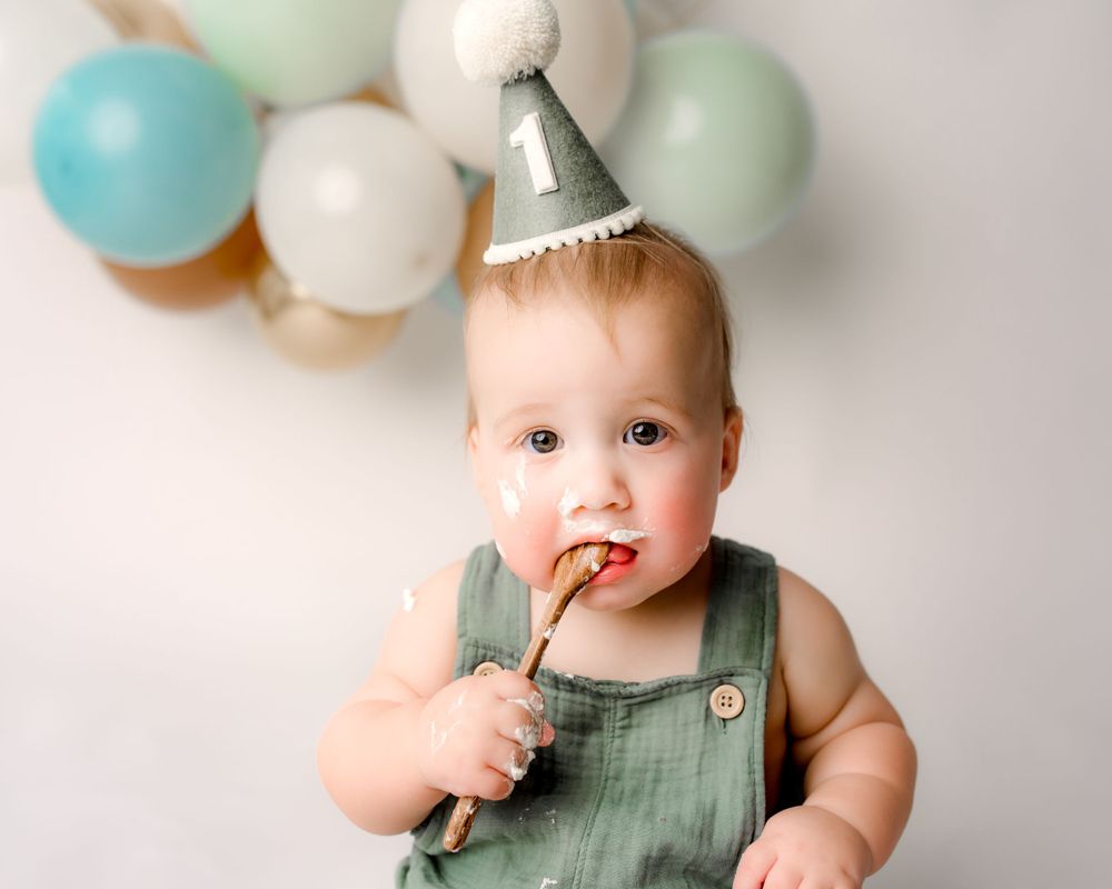 Baby with party hat eating first birthday cake | Three Little Bees Photography luxury milestone photographer