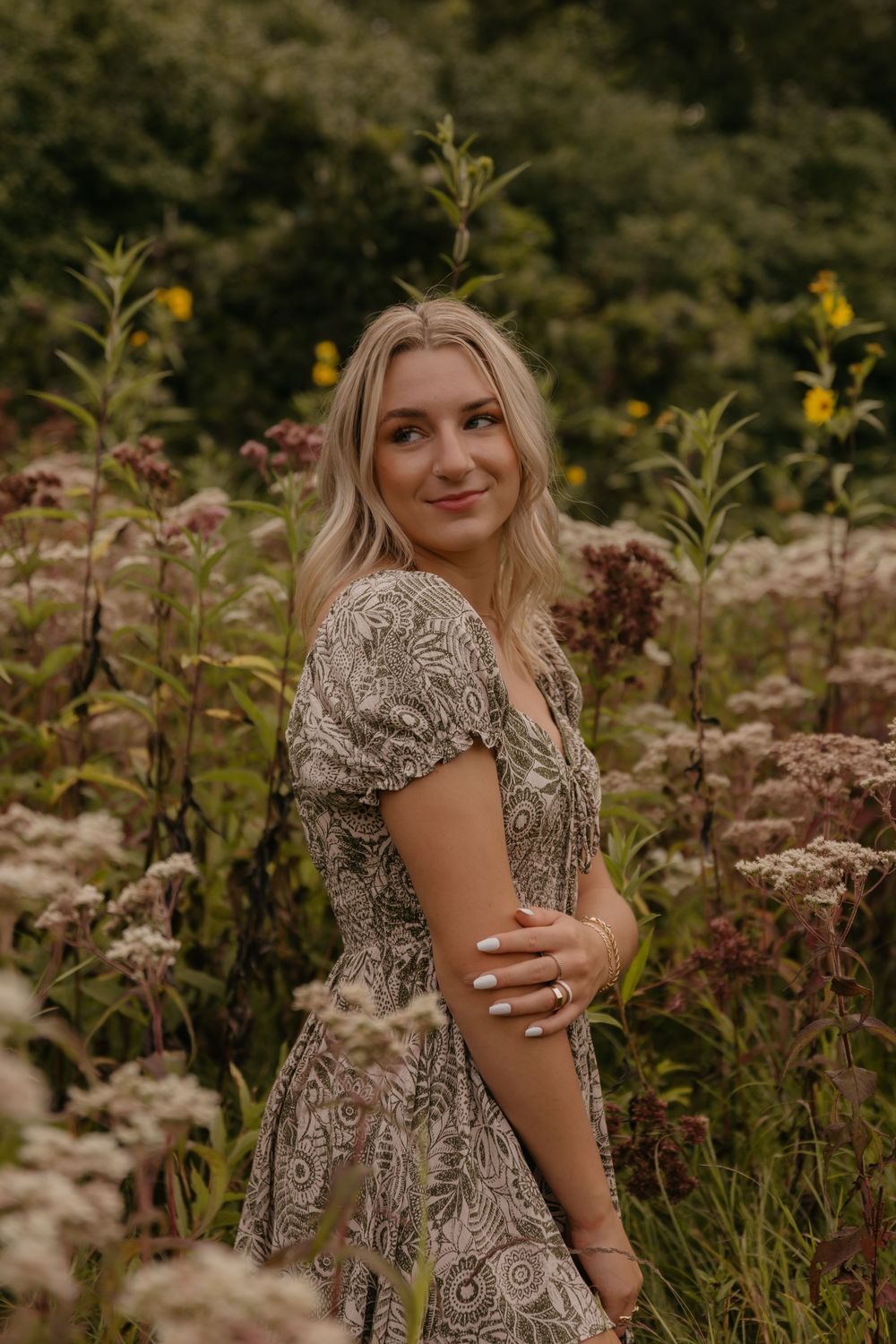 A woman in a floral dress poses in a field of wildflowers during golden hour.