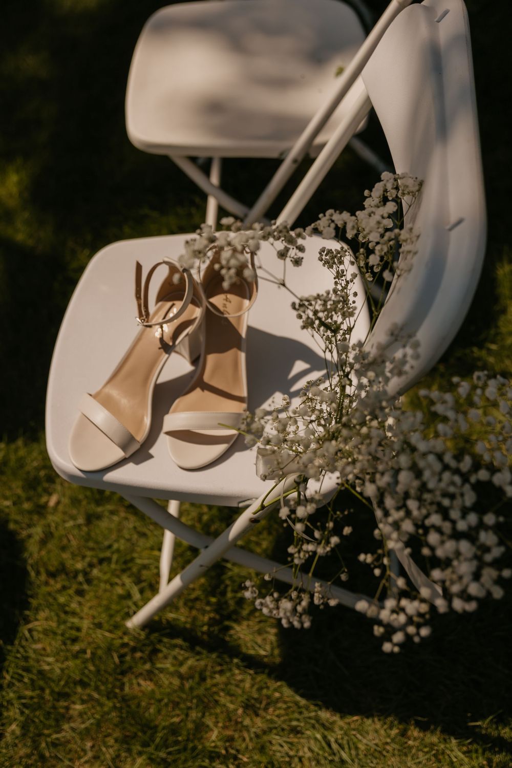 Wedding heels and baby's breath flowers arranged on white folding chair in natural light.