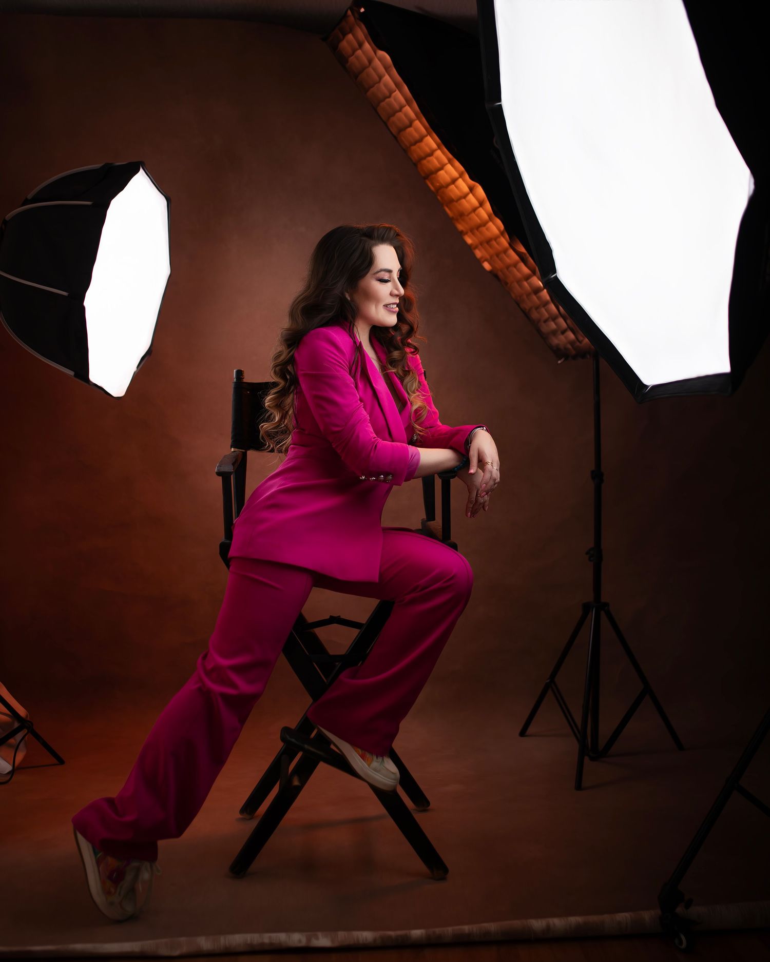 Woman in red blazer and distressed jeans poses on wooden ladder against brown backdrop.