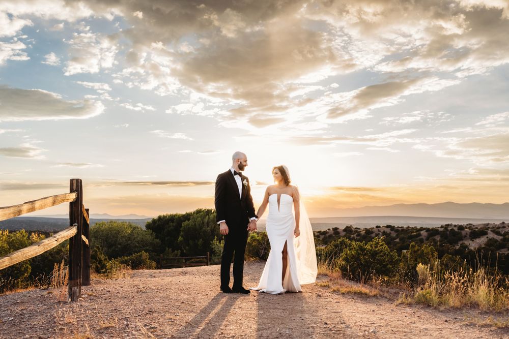 Married couple taking sunset photos in wedding attire at an overlook at the Four Seasons Resort in Santa Fe, New Mexico.