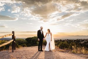 Married couple taking sunset photos in wedding attire at an overlook at the Four Seasons Resort in Santa Fe, New Mexico.