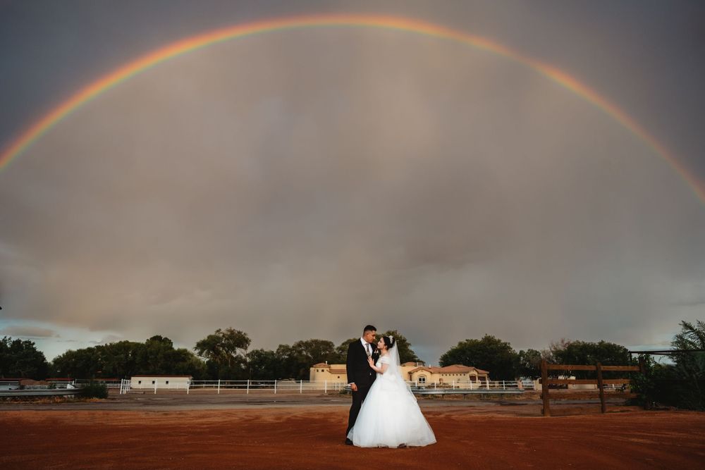 Huge rainbow across a moody sky with a small bridal couple for portraits in the South Valley of Albuquerque, New Mexico.