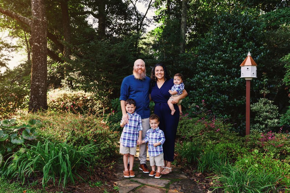 Family stands together on a wooded trail surrounded by lush greenery and ferns on a sunny afternoon.