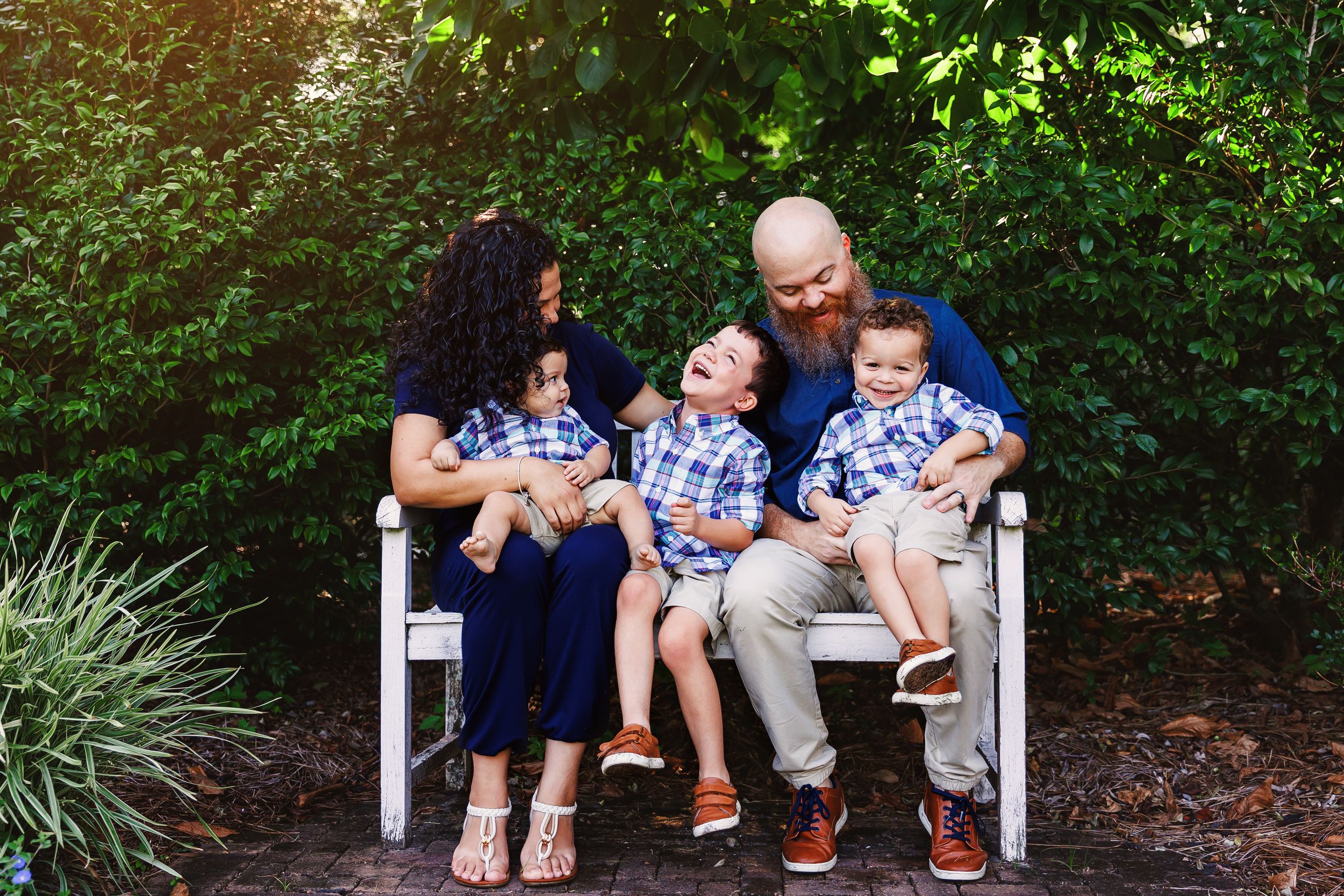 A family sits together on white benches in a lush garden setting, sharing intimate moments and conversations.