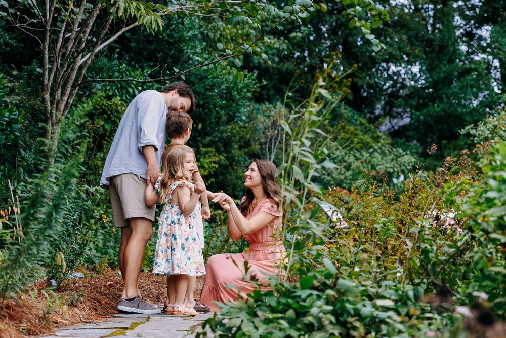 A couple enjoys a romantic outdoor picnic in a lush garden setting with wine glasses and food spread on a blanket.