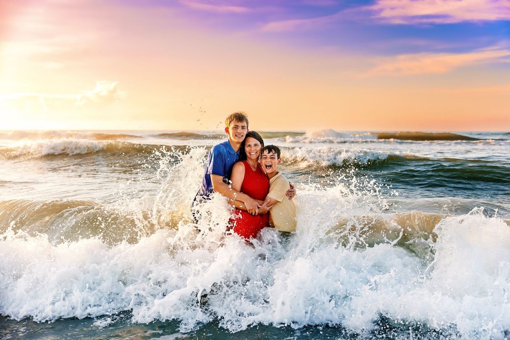 People playing in ocean waves during a vibrant sunset with crashing surf and colorful sky in the background.