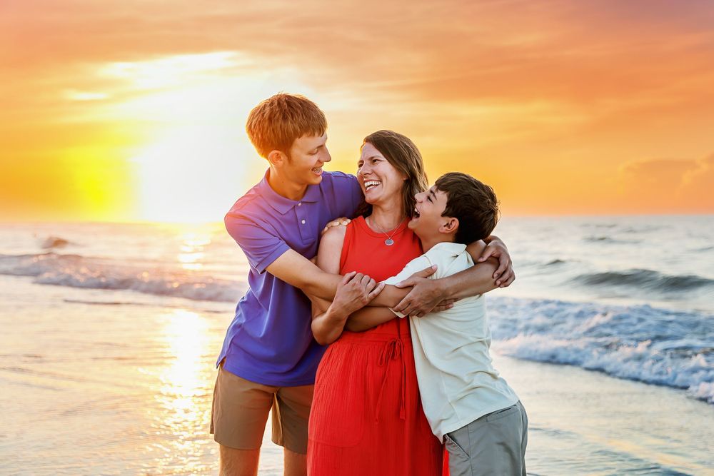 Couple embracing on beach at sunset with ocean waves and golden sky in background.