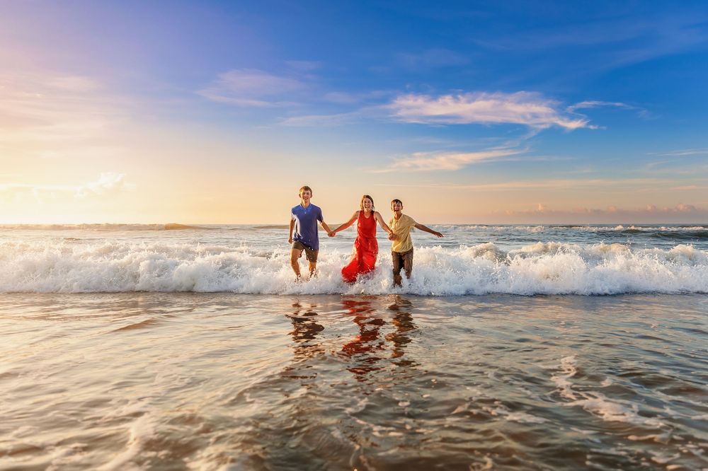 Three people holding hands while running through ocean waves at sunset on a beautiful beach.
