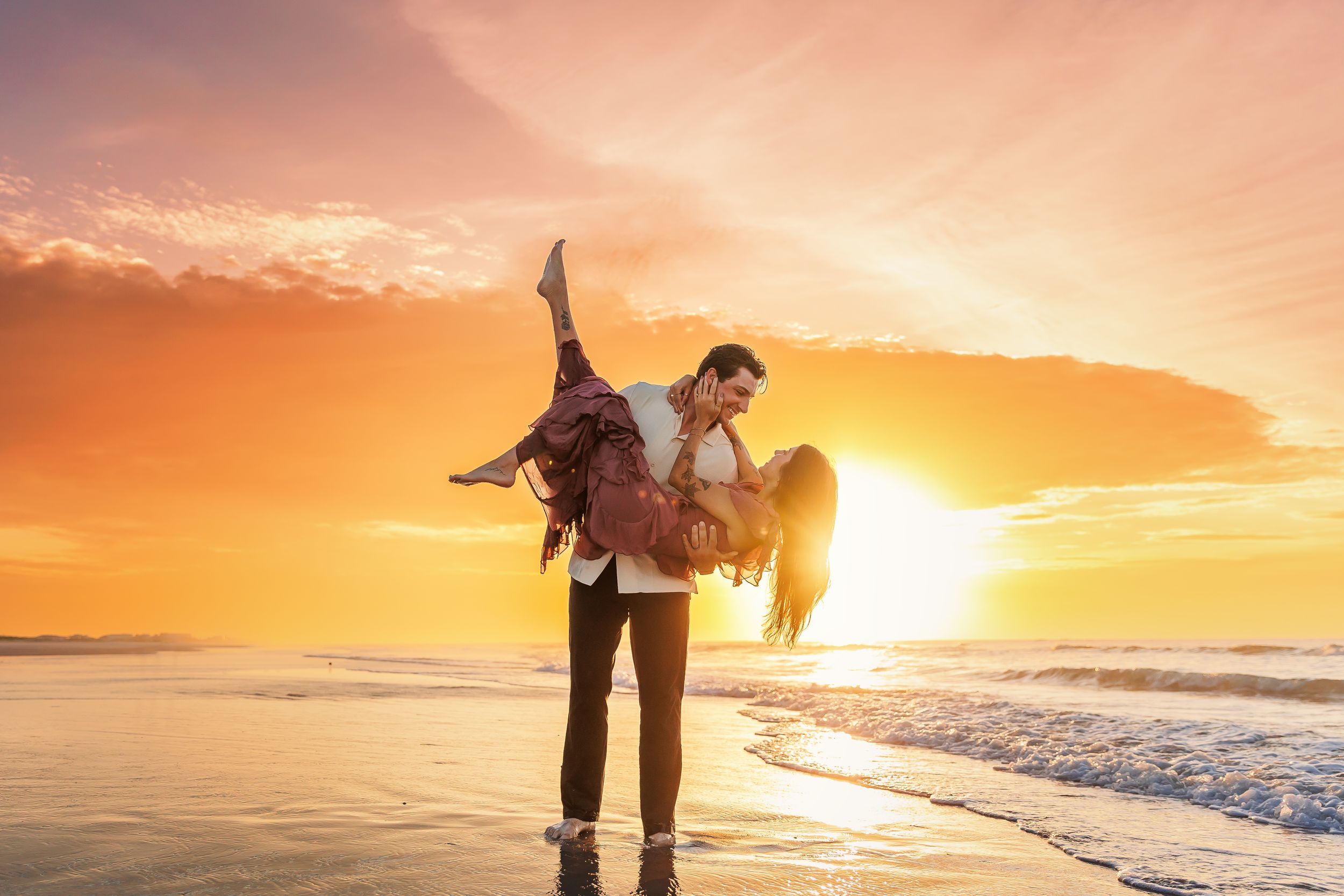 A couple walks hand in hand along a beach at sunset with golden light reflecting off the ocean waves.