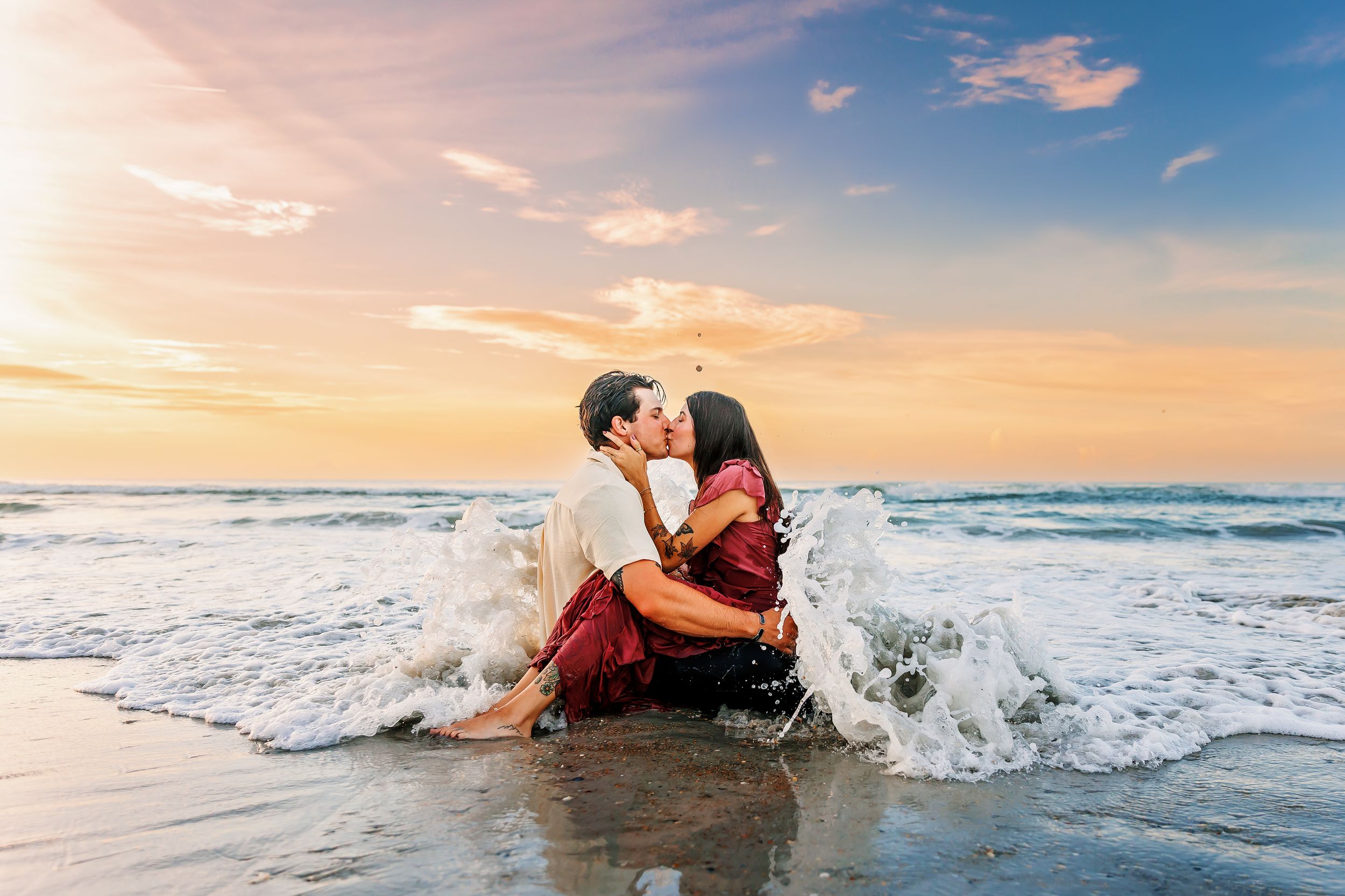 Couple in formal attire plays in ocean waves during golden hour photoshoot.