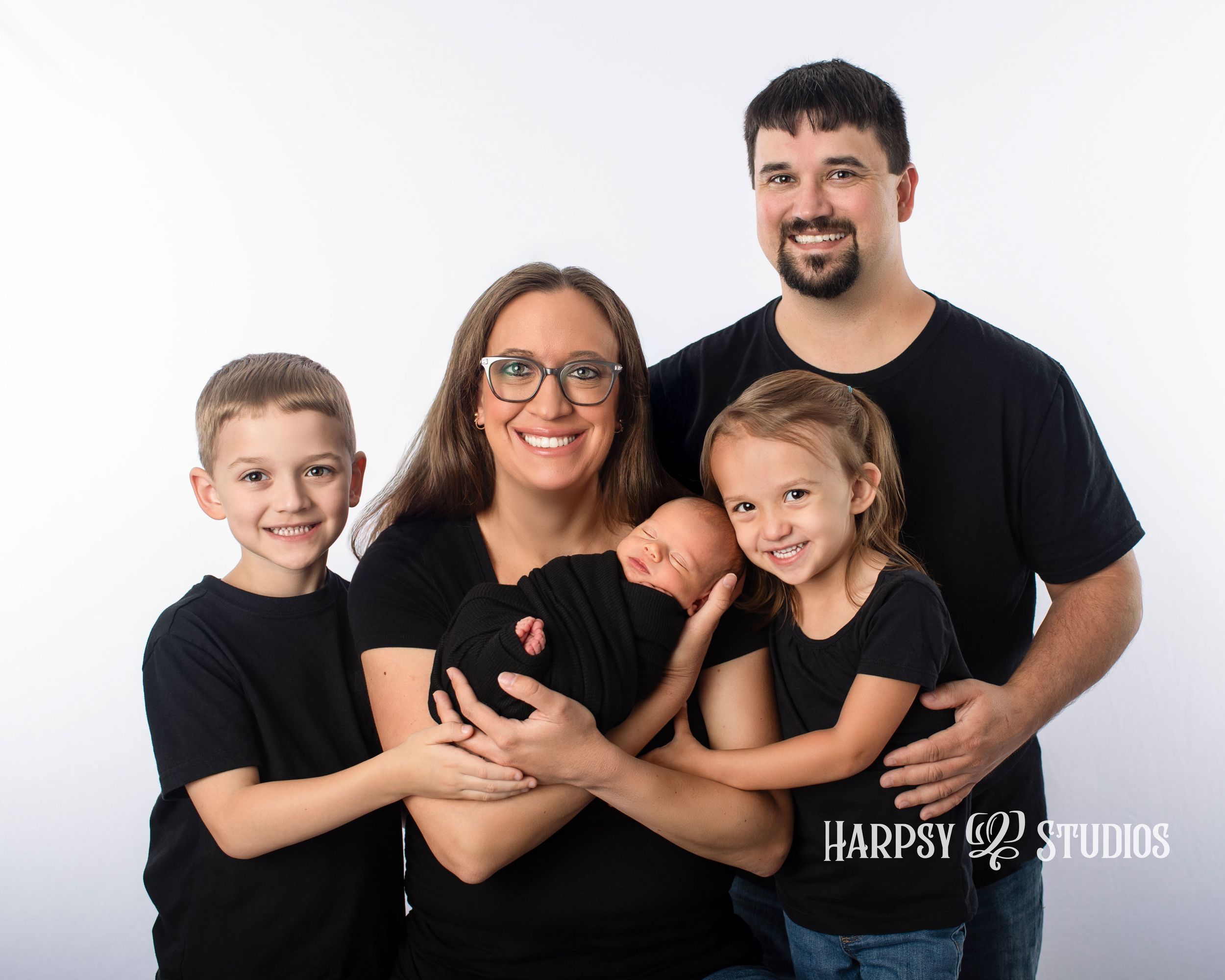 Family portrait during newborn photography session; family wearing black posed on white backdrop in professional portrait studio session